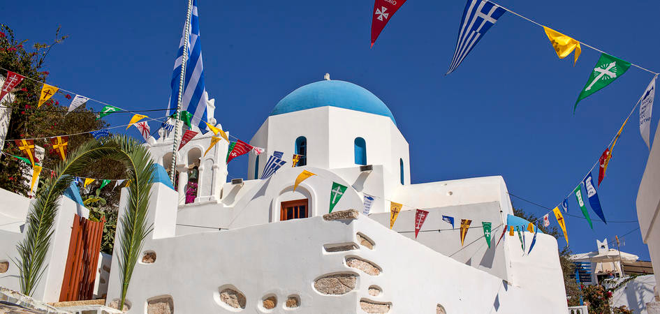 A classic white-washed Greek church with blue dome and bell stand