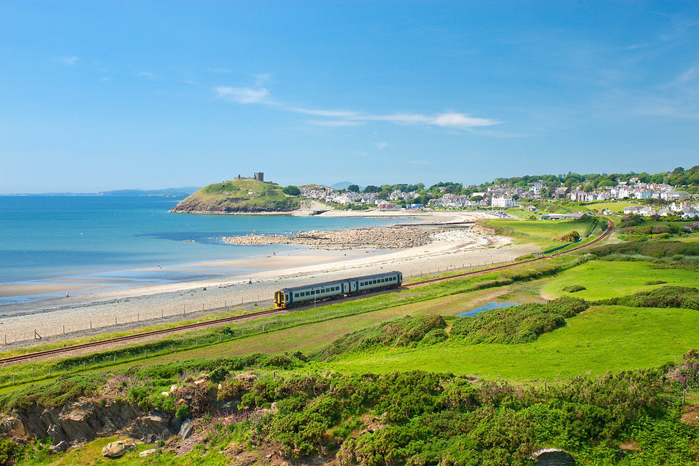 Train along coast with sea and ruined castle in background