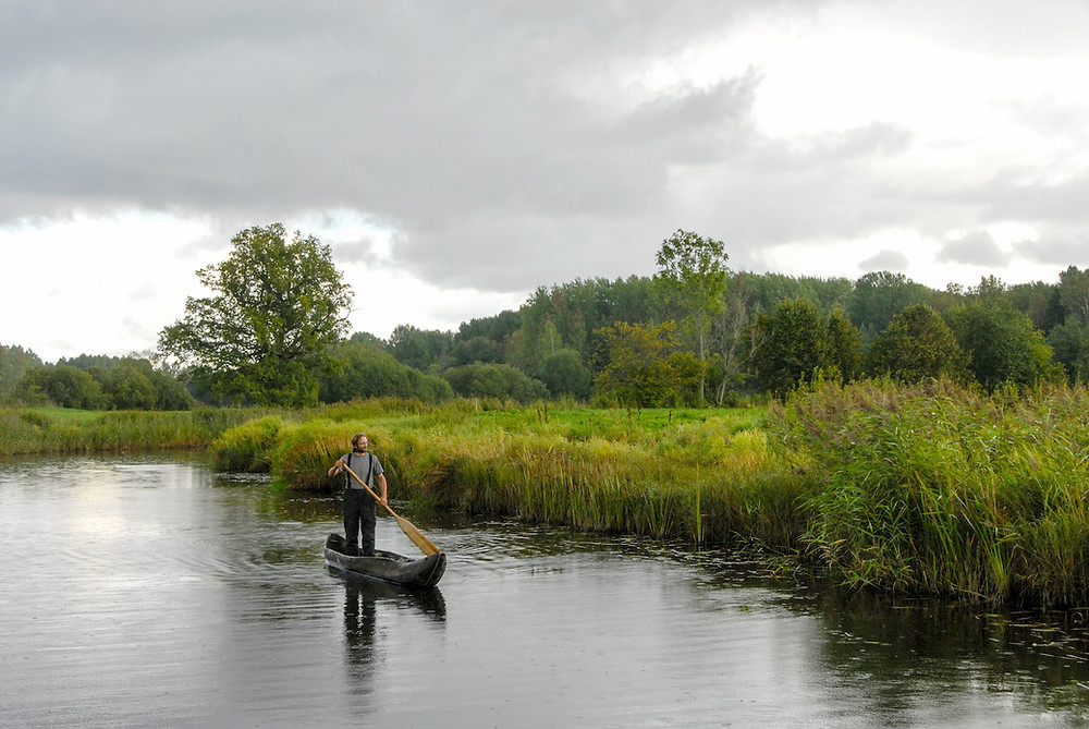 man with paddle in dug out canoe on river