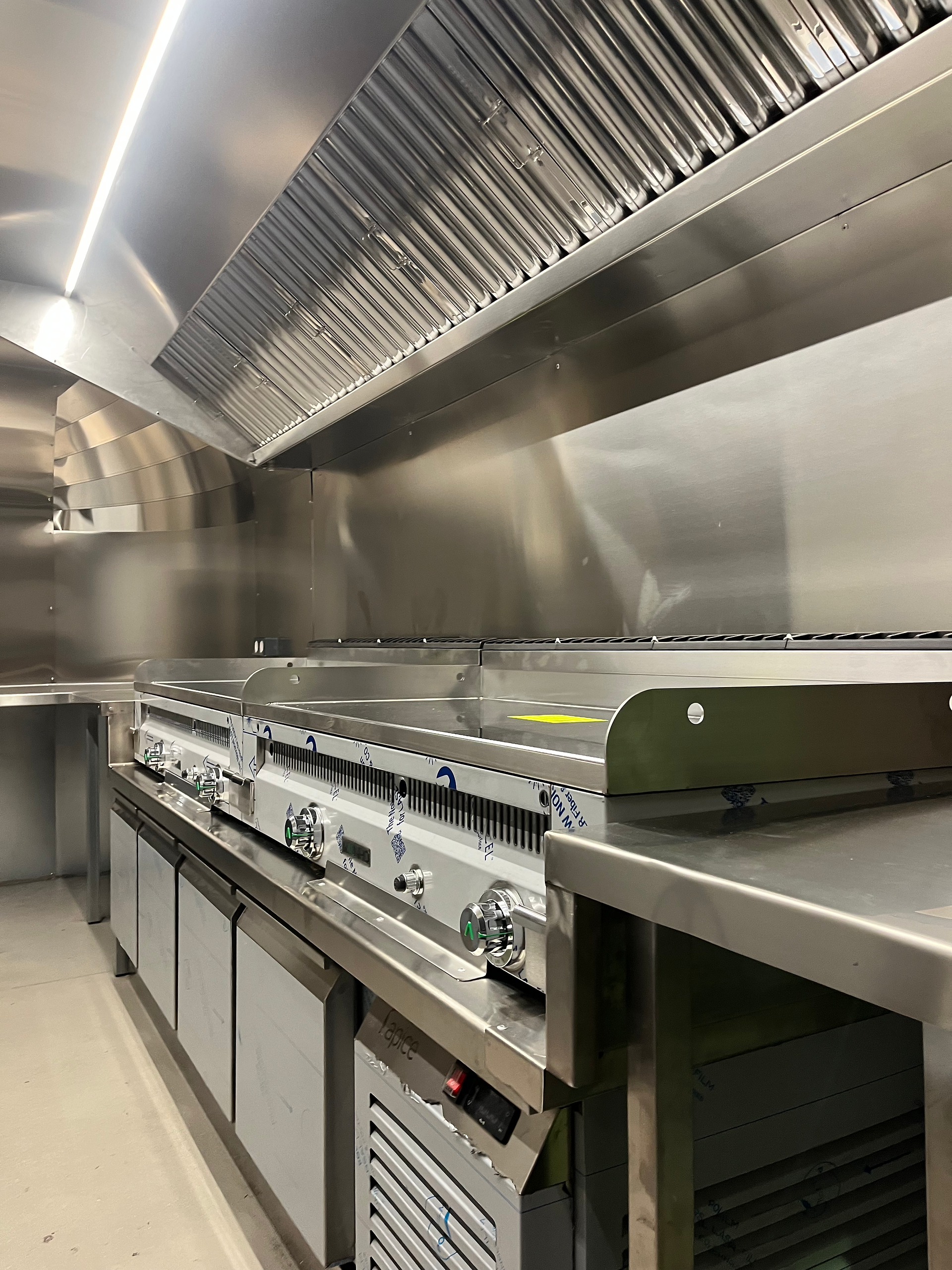 Interior de food truck con cocina de acero inoxidable, planchas y campana.