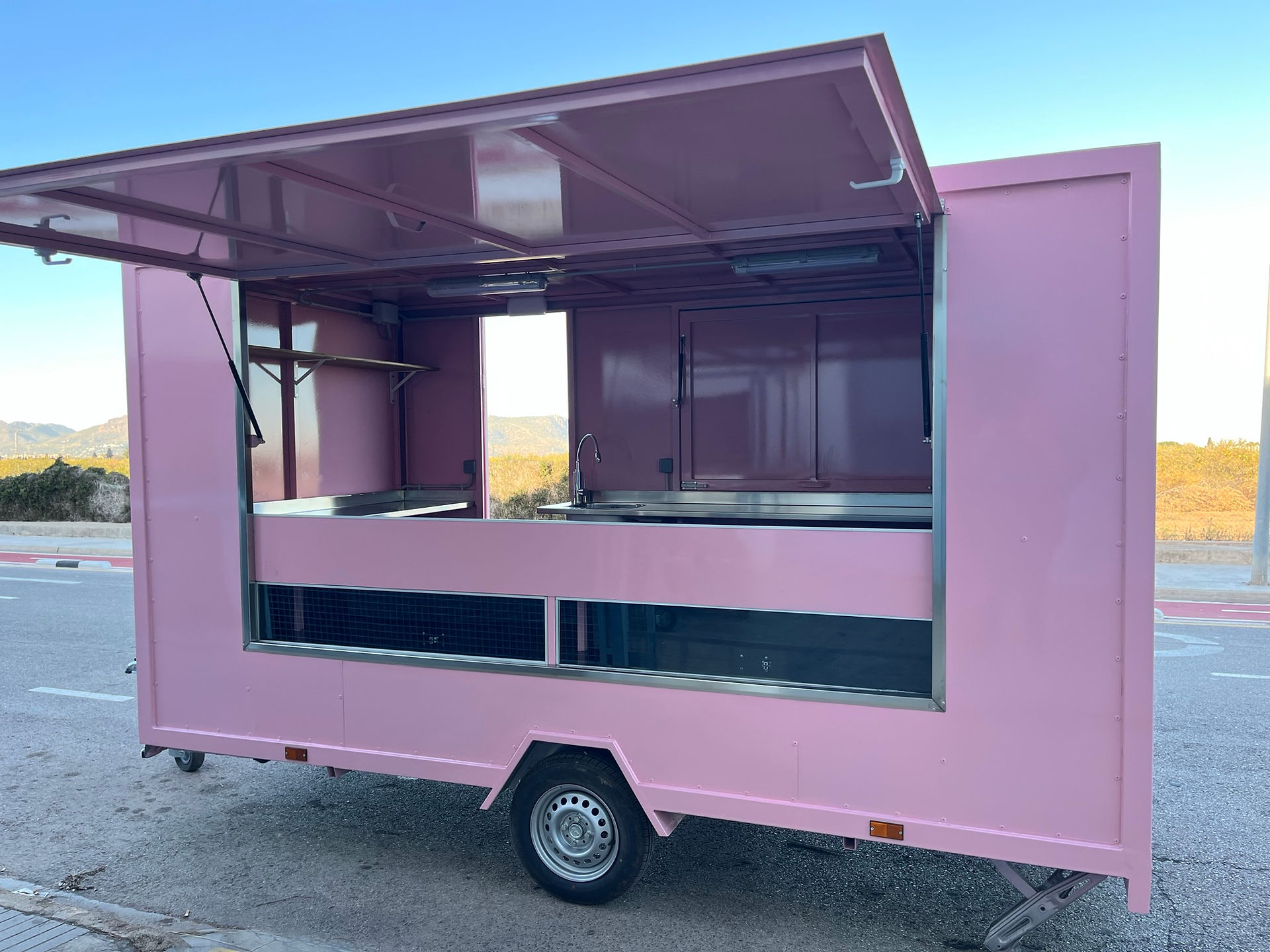 Remolque food truck rosa abierto con interior vacío, listo para operar.