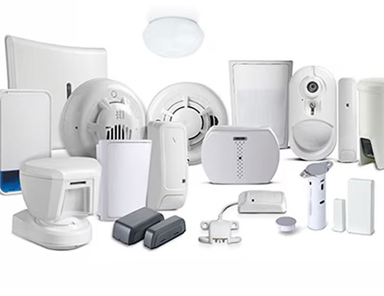 Eine Vielzahl von weißen und grauen, kabellosen Alarmsystemkomponenten, darunter Bewegungsmelder, Rauchmelder, Tür-/Fensterkontakte und Kameras, sind auf einem hellen Hintergrund angeordnet. Eine Deckenleuchte ist ebenfalls im Bild. Der Text lautet: 'Kabellos. Stromlos. Saubere Installation.' und 'Rufen Sie uns an!'. Das Bild betont die einfache und unauffällige Installation moderner, drahtloser Sicherheitssysteme.