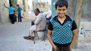 A boy smiling with an older man sitting in the background