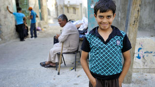 A boy smiling with an older man sitting in the background