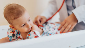 A baby lying on an exam table in a clinic being examined with a stethoscope