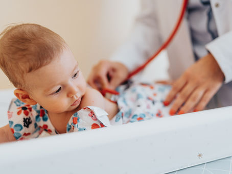 A baby lying on an exam table in a clinic being examined with a stethoscope