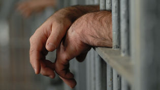 A man's hands outside the bars of a prison cell