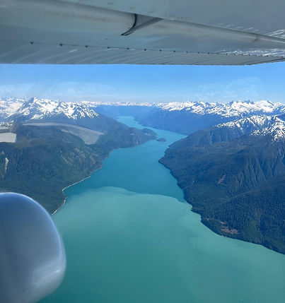 Flying over snow-capped mountains and a turquoise lake seen from an airplane in Alaska