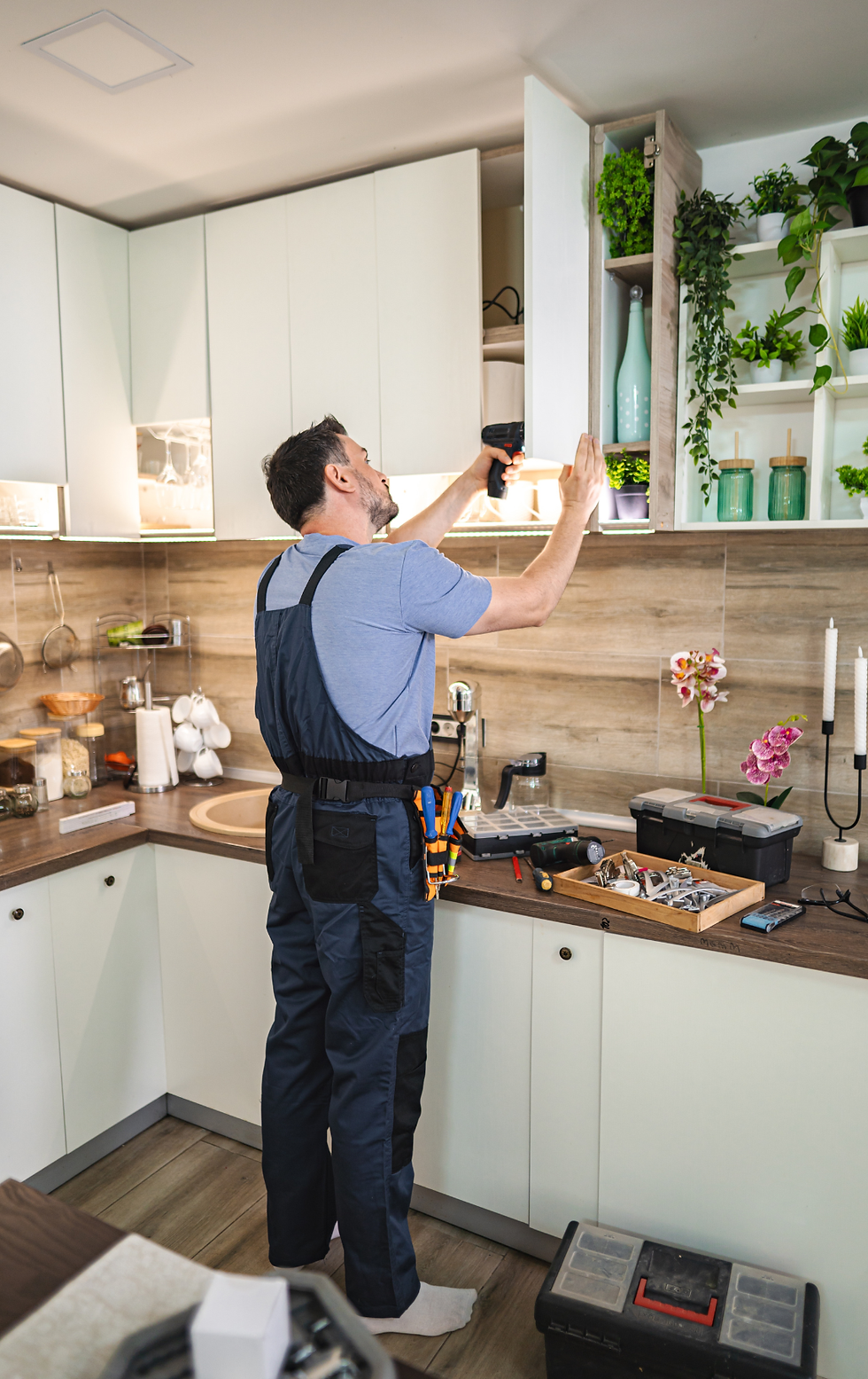 Handyman installing kitchen cabinets using electric screwdriver