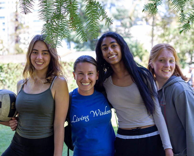 A group of four smiling teenage girls standing together outdoors, representing a supportive school community.