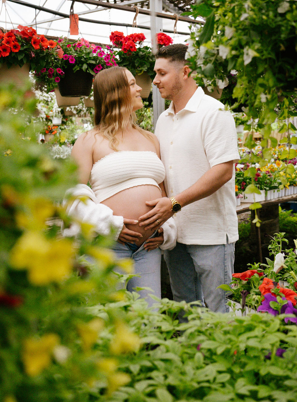 Expecting parents in a vibrant Ontario greenhouse maternity shoot, surrounded by lush plants and playful energy, captured with personality and warmth.