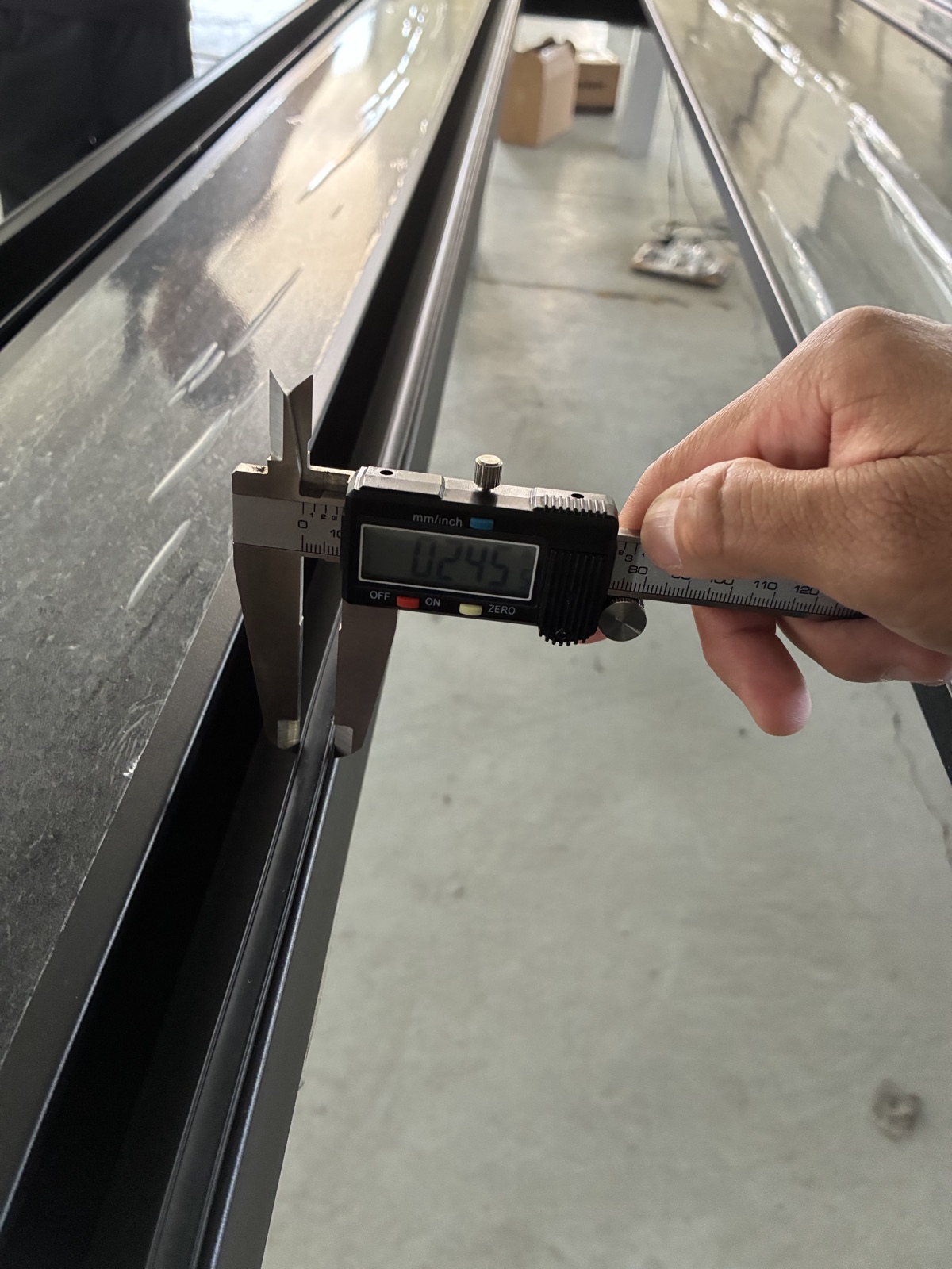 A digital caliper checking the thickness of an aluminum profile at the factory