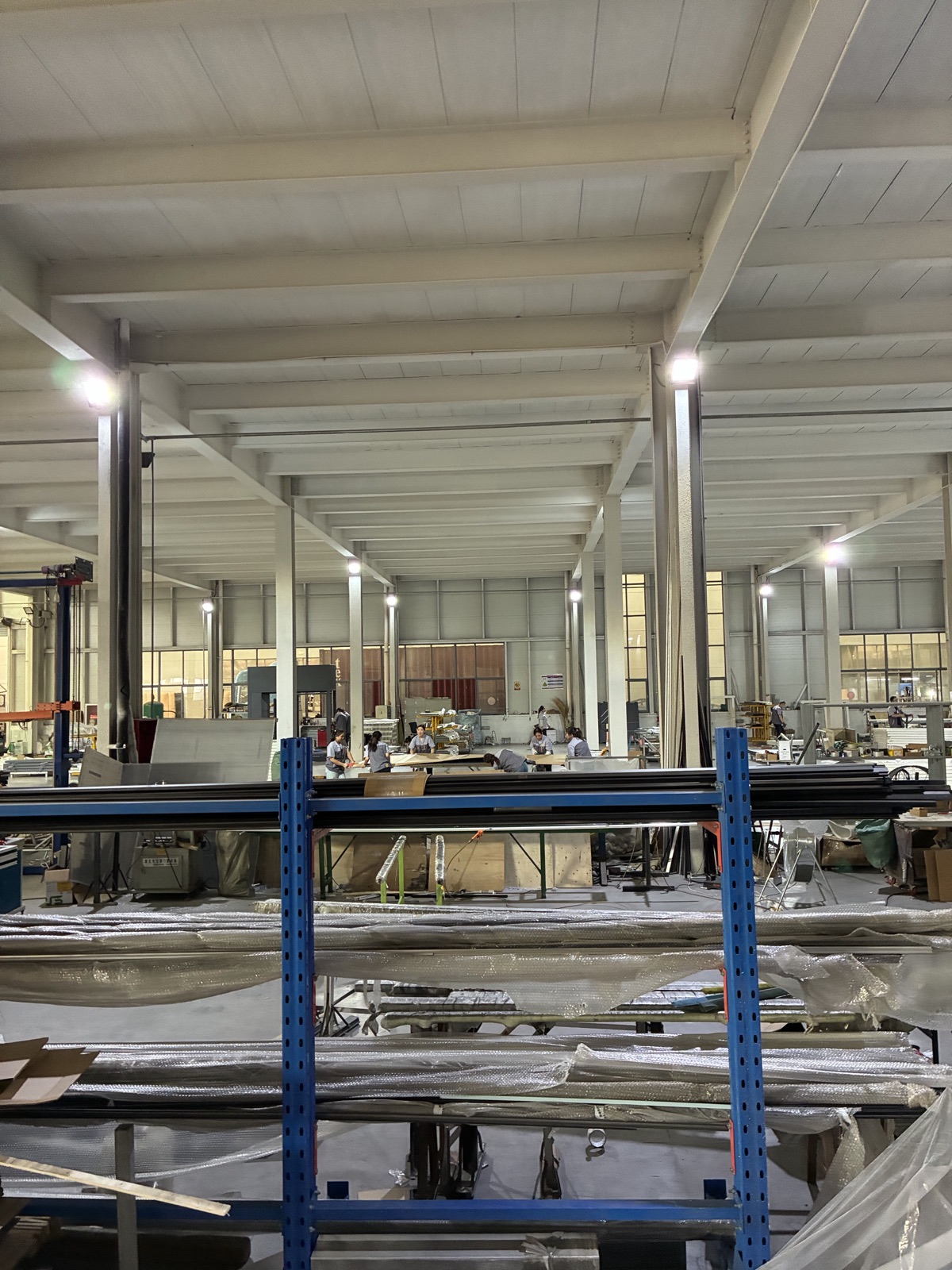 A long production hall with racks of aluminum profiles and workers at their stations