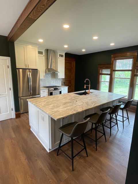 modern farmhouse kitchen remodel. Big island with white cabinets and natural wood grain trim and dark walls. 