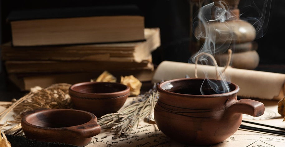 Mystical ritual setup with smoking clay pot, ancient spellbooks, magical symbols, herbs, and feathers used in traditional cur