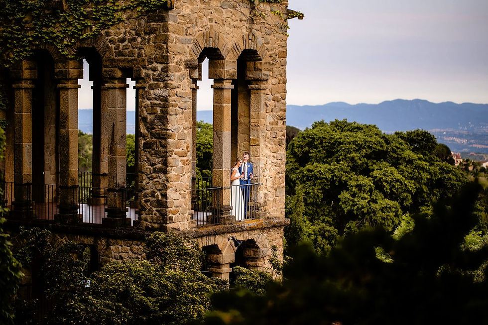 A bride and groom sharing a toast on the iconic stone balcony of La Baronia, featuring Gothic arches and a panoramic view of the Catalan mountains near Barcelona.