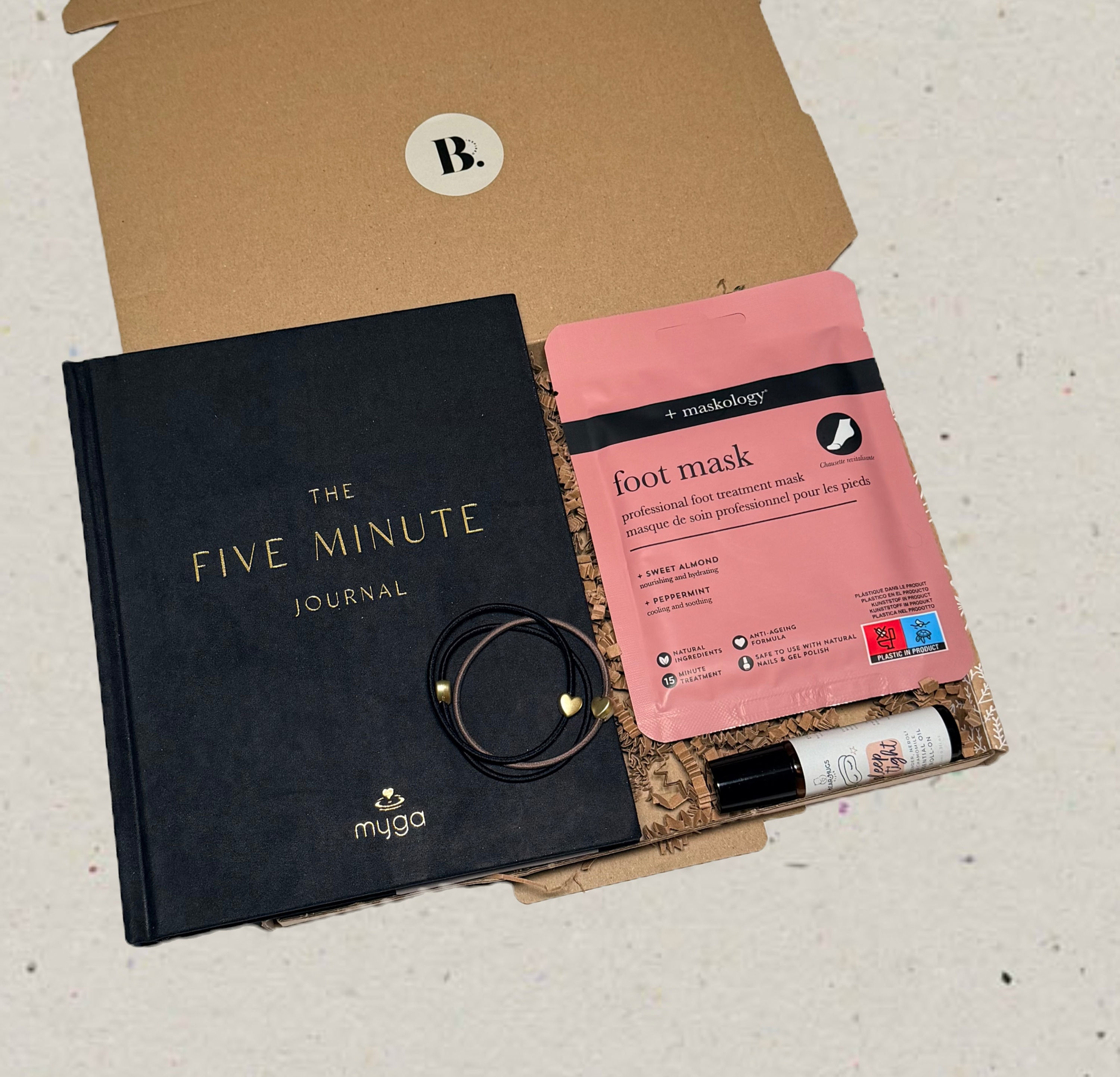 Gift box that includes: five minute journal, foot mask, hair bands and essential oil roller