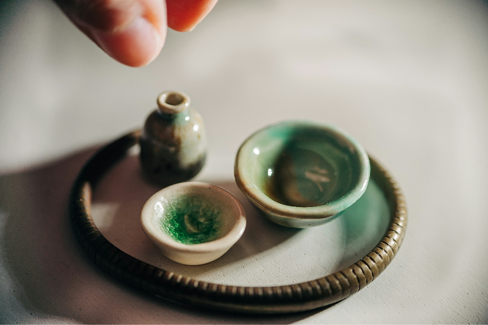 A tiny tray with tiny pottery pieces - a vase and two tiny bowls in pale green colours.