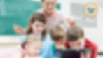 A teacher leans over students to help or observe students working on a computer in a classroom setting.