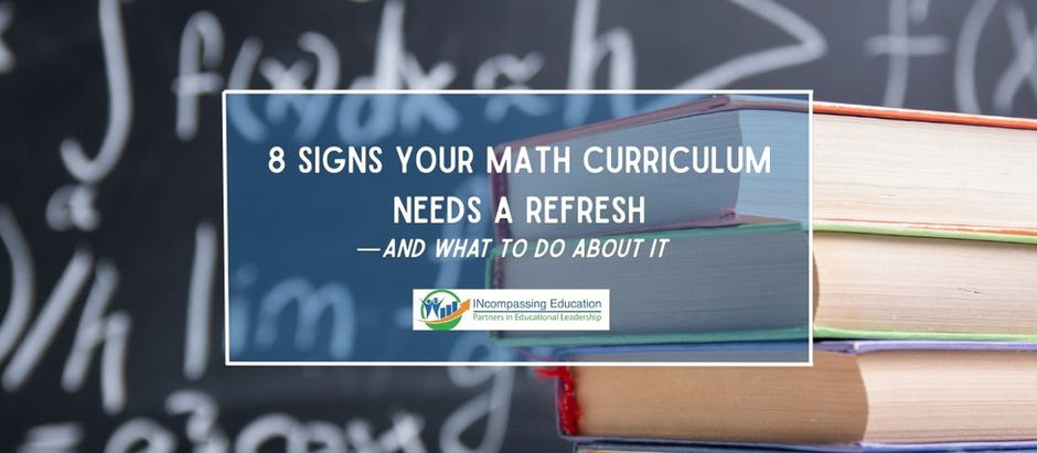 A stack of textbooks sits in front of a black board with math formulas written on the board.