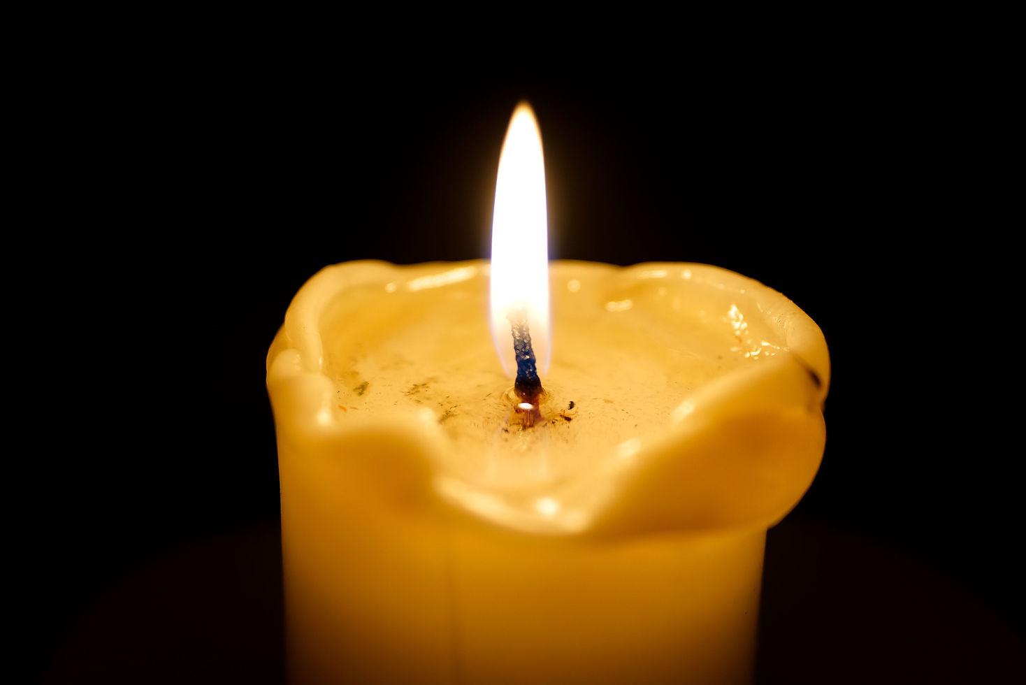 Close-up of a steady candle flame and wick against a dark background.