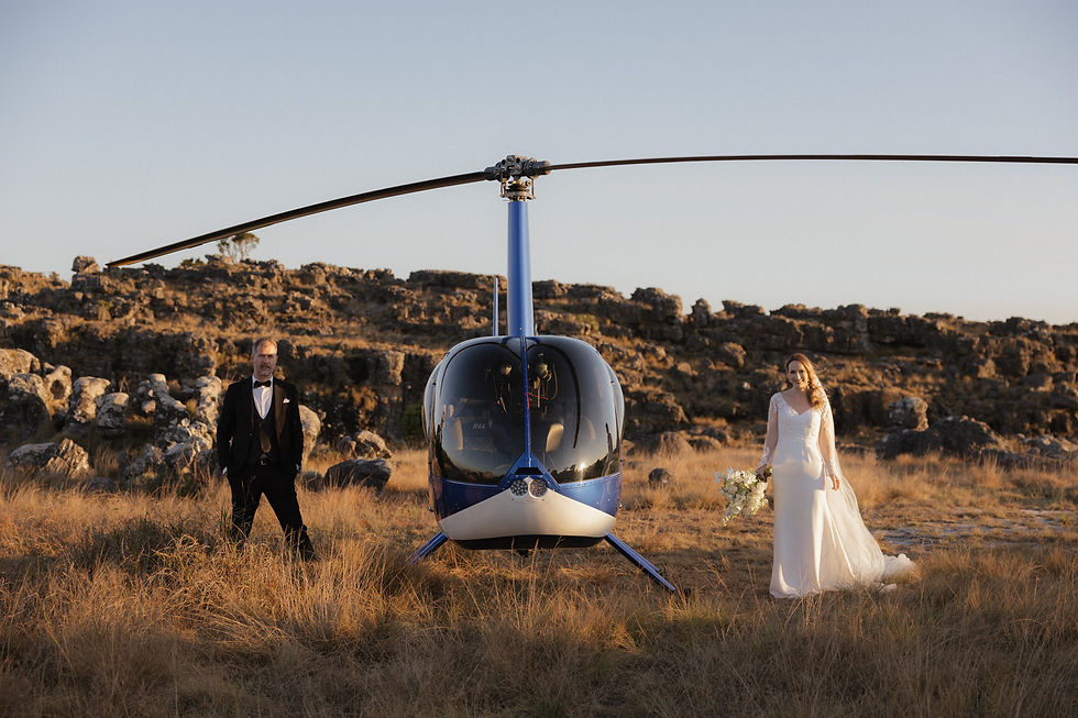 Bride and groom standing beside blue helicopter during South Africa elopement in rocky Panorama Route landscape