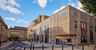 Exterior of Bolton Octagon Theatre, with brown brick, a silver sign and yallow window coverings above the main door