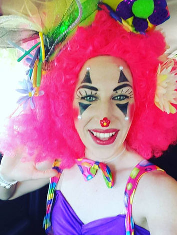 Clown with pink hair smiling in a car with colorful accessories