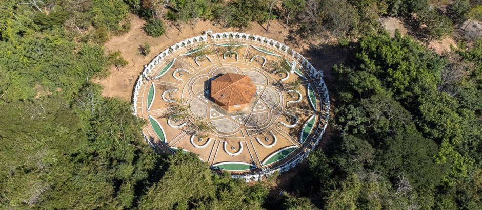 Fotografia aérea do Mandala dos Anjos construída em Chapada dos Guimarães em meio a floresta típica da região tendo ao centro um edificação hexagonal e ladeada por estátuas dos 72 anjos.