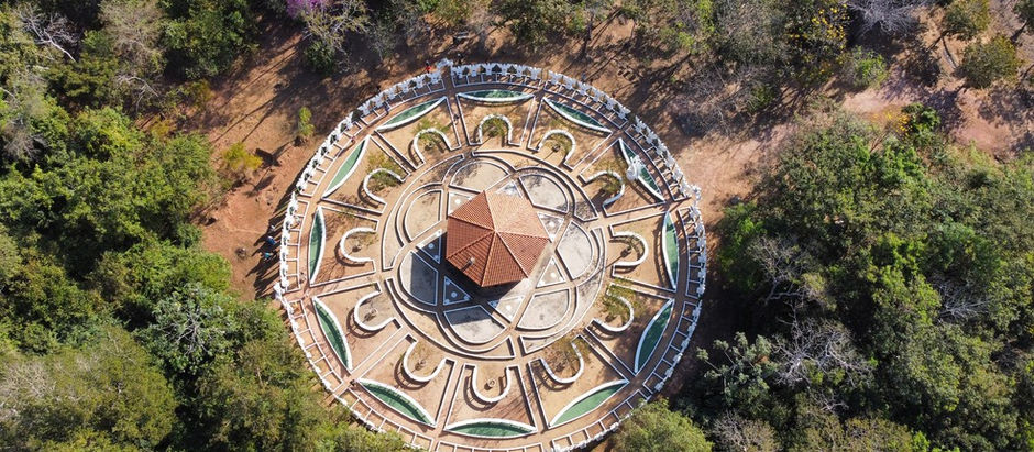 Fotografia aérea do Mandala dos Anjos construída em Chapada dos Guimarães em meio a floresta típica da região tendo ao centro um edificação hexagonal e ladeada por estátuas dos 72 anjos.