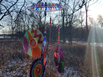 Colorful CDs hanging like a windchime glisten in the sunlight against a snowy forest backdrop, creating a serene, reflective mood.
