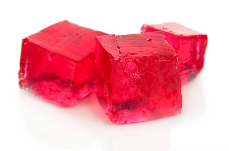 Three red gelatin cubes on a white surface, glistening with a shiny texture. No text or additional elements present.