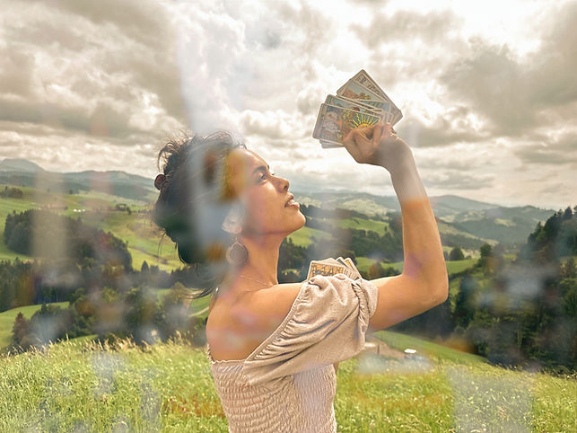 Isabella Pörschke von Bellas Tarot Beratung steht in der Natur, hält Tarotkarten und blickt hoffnungsvoll auf sie, weiter Himmel im Hintergrund