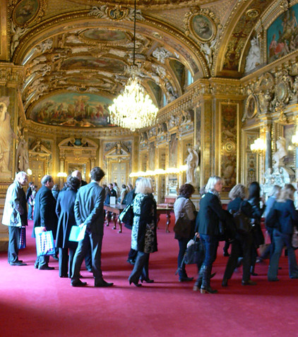 Groupe de personnes visitant une salle dorée, plafond richement décoré au Louvre.