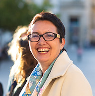 Femme souriante, lunettes, manteau beige. Groupe de personnes en arrière-plan.