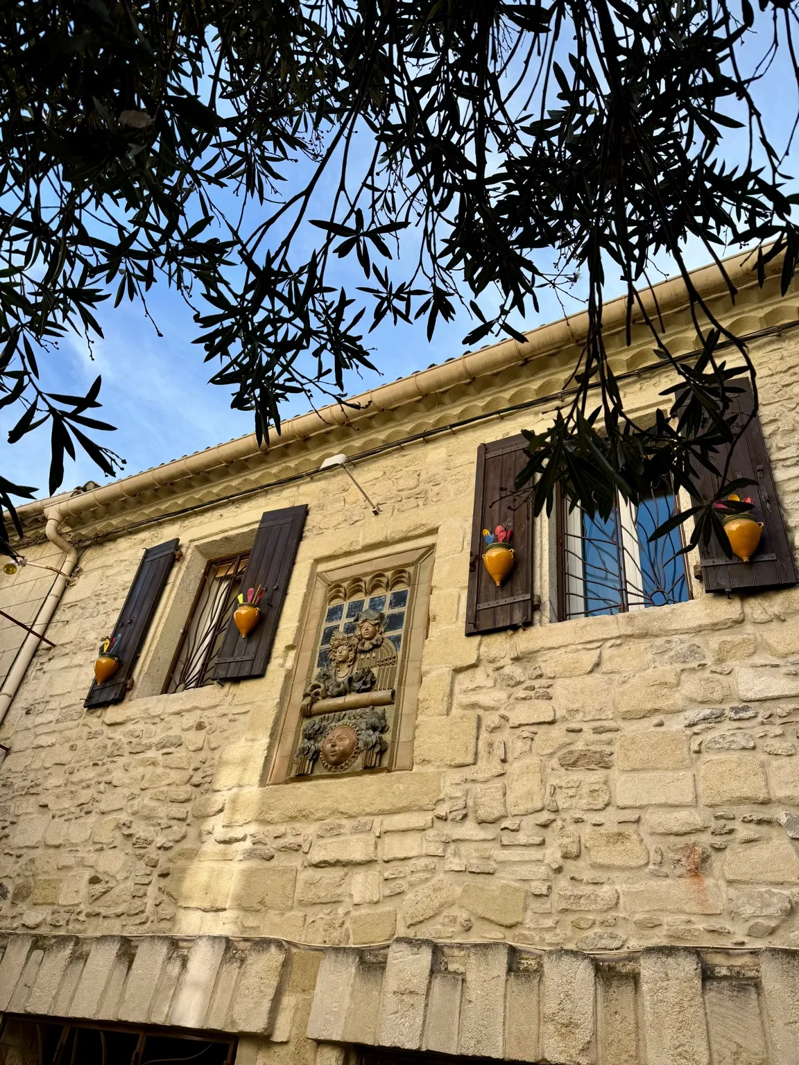 Kamienny budynek w Camargue z ozdobnym oknem i ceramicznymi donicami przy okiennicach.