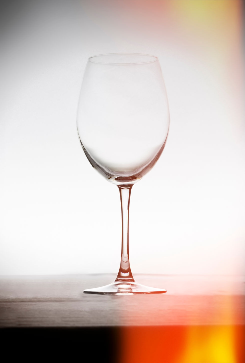 Empty wine glass stands alone on a dark surface against a white backdrop.