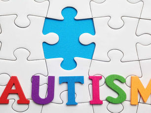 Puzzle pieces form a background with a single blue piece missing. Colorful wooden letters spell "AUTISM" at the bottom.