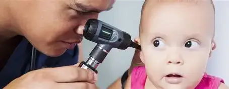 Pediatric Audiologist examines a baby’s ear with an otoscope; the baby looks wide-eyed and surprised in a close-up clinic scene.
