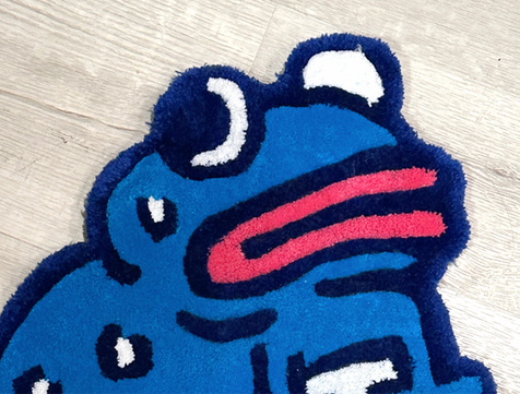 A photo of a rug shaped like a blue frog against a grey wooden floor.