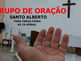 UMA MÃO MOSTRANDO INFORMAÇÕES SOBRE GRUPO DE ORAÇÃO COM UMA CRUZ NA PAREDE