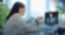 Woman in white jacket video calls on a laptop in a bright office, gesturing toward the screen; CLEARDESK logo visible.