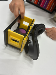 Hands assembling a yellow and black 3D-printed object.