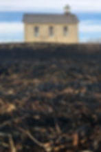 Burned prairie field with historic limestone schoolhouse under open sky in Kansas