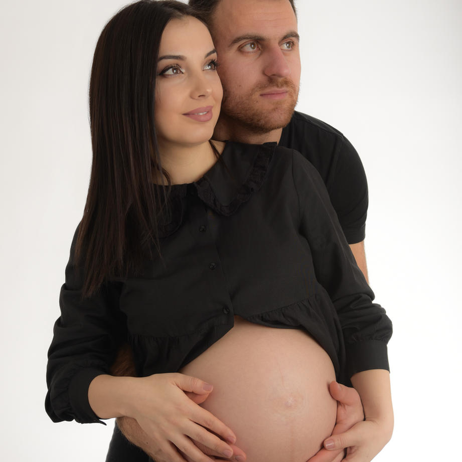Mum and dad to be wearing black. Mum is showing her baby bump and both have their hands on her bump.