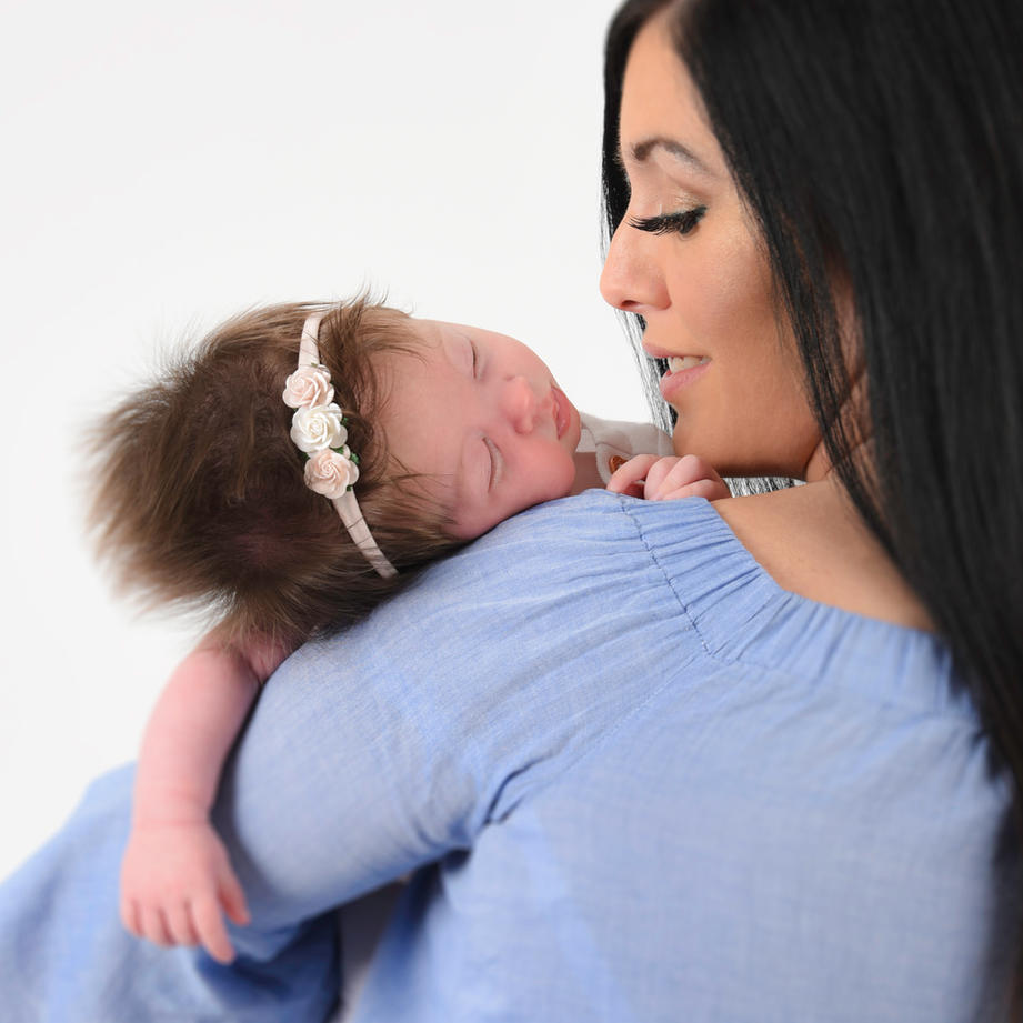 New mum with her back to us. Holding her baby on her shoulder. Mum is smiling at her baby and she has long dark hair.