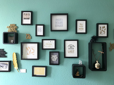 Martina's Arbeitszimmer ist in einem Salbeigrün gehalten und mit weißen Möbeln. Lediglich die Bilderwand über dem Schreibtisch zeigt unterschiedliche Rahmenformate, kombiniert mit Schwarz und Gold.