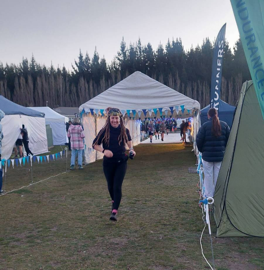 A smiling runner runs towards the camera after coming out of a white gazebo.