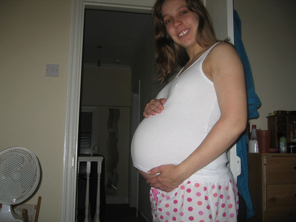A pregnant lady stands sideways holding her pregnant bump.