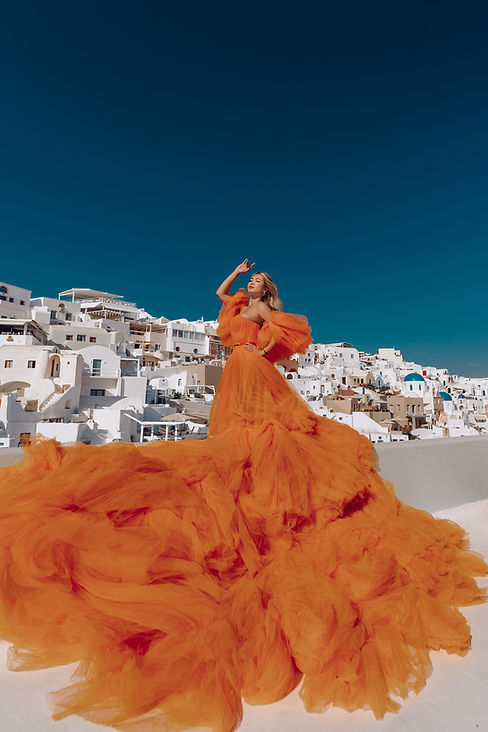 Girl in orange cloud dress in Santorini near blue domes jn Oia